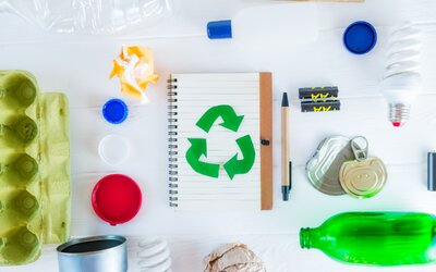 Bunte Recycling-Symbolkarte, Stifte, Papier, Flaschen und Behälter auf hellem Untergrund