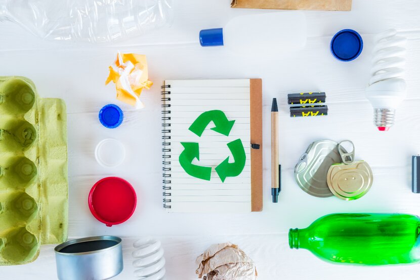 Bunte Recycling-Symbolkarte, Stifte, Papier, Flaschen und Behälter auf hellem Untergrund